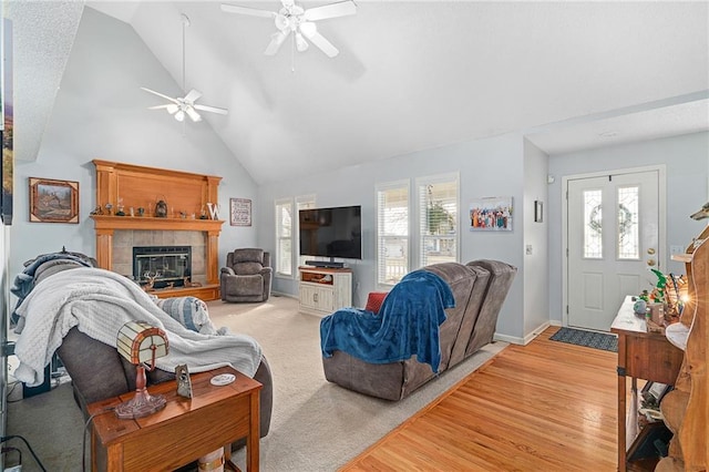 living area with baseboards, high vaulted ceiling, a fireplace, ceiling fan, and light wood-style floors