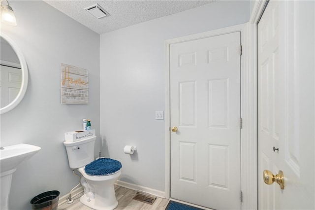 half bathroom with visible vents, baseboards, a textured ceiling, and toilet