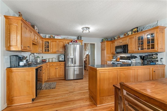 kitchen featuring dark countertops, glass insert cabinets, light wood-type flooring, a peninsula, and black appliances