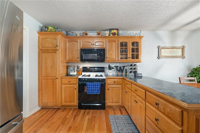 kitchen with light wood-type flooring, freestanding refrigerator, range with gas cooktop, black microwave, and glass insert cabinets