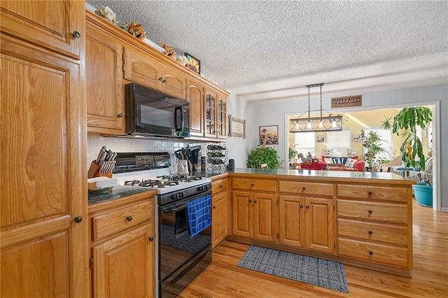 kitchen with a peninsula, gas stove, light wood-style floors, and black microwave