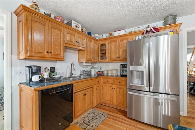 kitchen with glass insert cabinets, black dishwasher, light wood-style floors, stainless steel fridge, and a sink