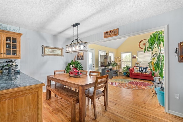 dining room with baseboards, a textured ceiling, light wood-style flooring, and vaulted ceiling