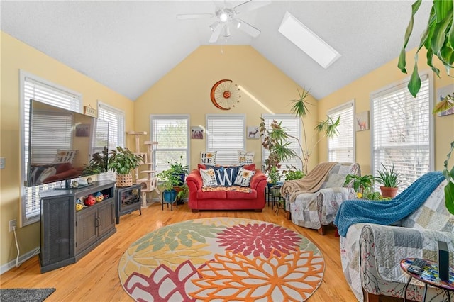 living area with high vaulted ceiling, light wood-style floors, a skylight, and a ceiling fan