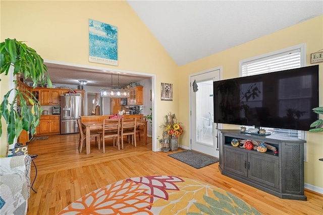 living room featuring a chandelier, baseboards, light wood finished floors, and high vaulted ceiling