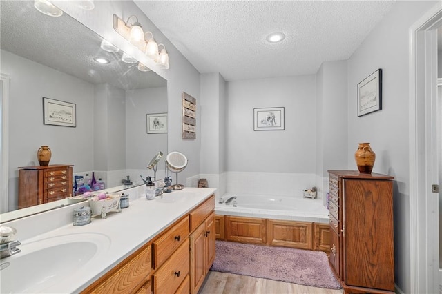 bathroom featuring a bath, wood finished floors, a textured ceiling, and a sink