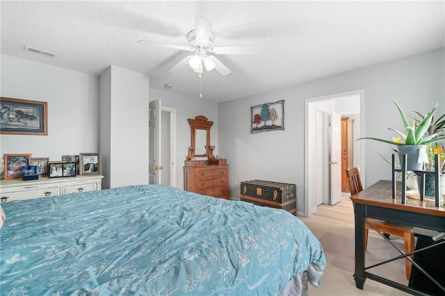 bedroom featuring light carpet, visible vents, a textured ceiling, and a ceiling fan