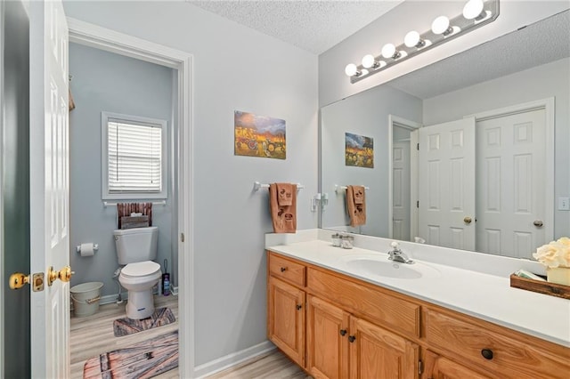 bathroom featuring baseboards, toilet, vanity, wood finished floors, and a textured ceiling