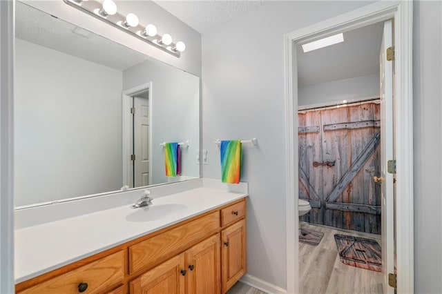 bathroom with toilet, vanity, a shower with curtain, wood finished floors, and a textured ceiling