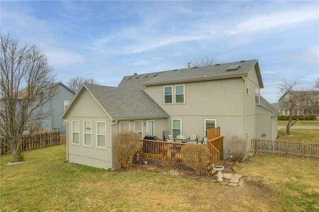 back of house featuring a wooden deck, a lawn, a shingled roof, and fence