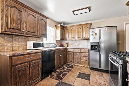6745 Cleveland Ave, Kansas City, MO 64132 - kitchen with backsplash, stainless steel appliances, light tile patterned flooring, and light countertops