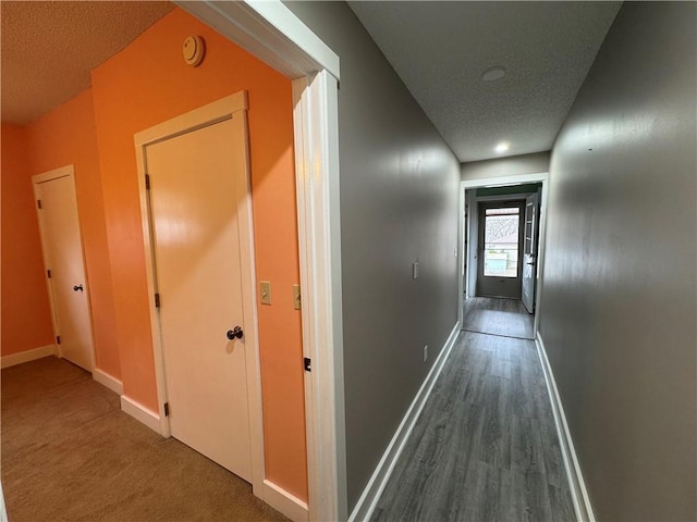 hall with dark wood finished floors, a textured ceiling, and baseboards