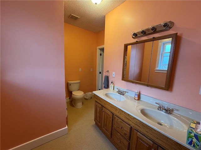 bathroom with a textured ceiling, double vanity, toilet, and a sink