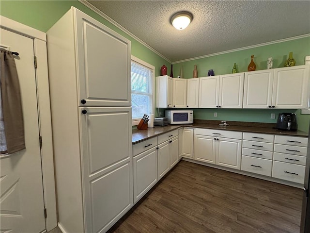 kitchen with white microwave, ornamental molding, dark wood-style flooring, and white cabinetry