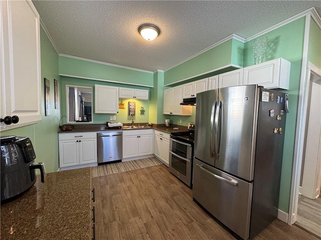 kitchen with stainless steel appliances, dark countertops, wood finished floors, and crown molding