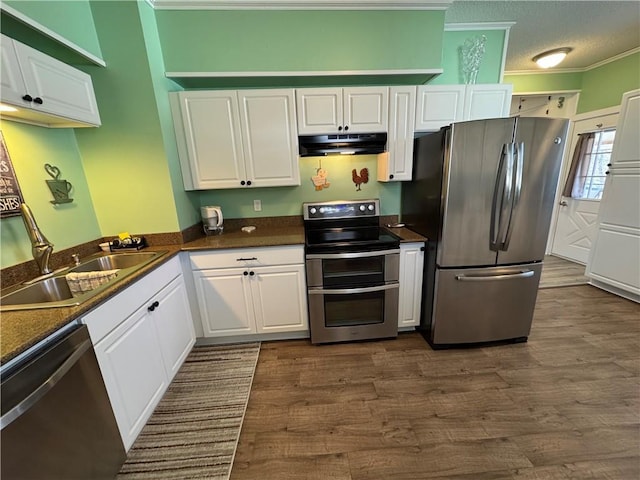 kitchen featuring dark countertops, a sink, under cabinet range hood, stainless steel appliances, and dark wood-style flooring