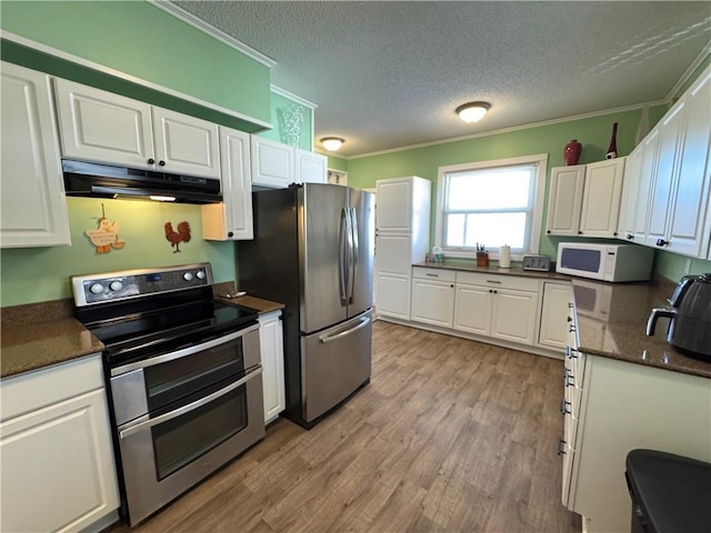 kitchen featuring ornamental molding, under cabinet range hood, dark countertops, white cabinetry, and appliances with stainless steel finishes