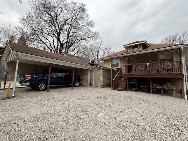 exterior space with an attached carport, stairway, gravel driveway, a shingled roof, and an outdoor structure