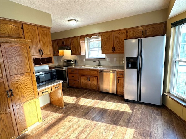 kitchen with backsplash, hardwood / wood-style floors, brown cabinets, appliances with stainless steel finishes, and a sink