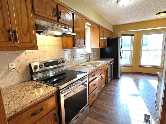 kitchen with appliances with stainless steel finishes, brown cabinets, under cabinet range hood, and a sink