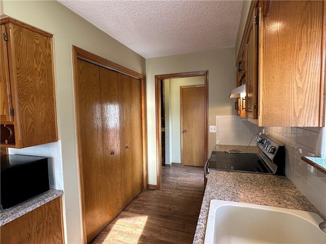 kitchen featuring electric stove, a sink, under cabinet range hood, dark wood-style floors, and light countertops