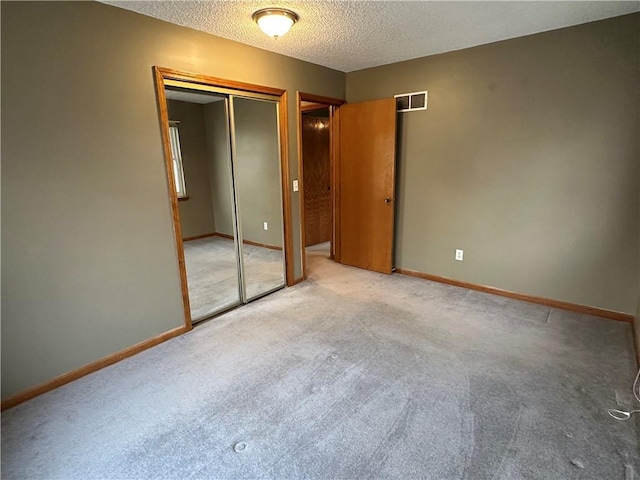 unfurnished bedroom with a closet, light colored carpet, a textured ceiling, and baseboards