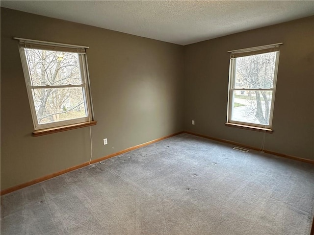 unfurnished room featuring baseboards, a healthy amount of sunlight, visible vents, and a textured ceiling