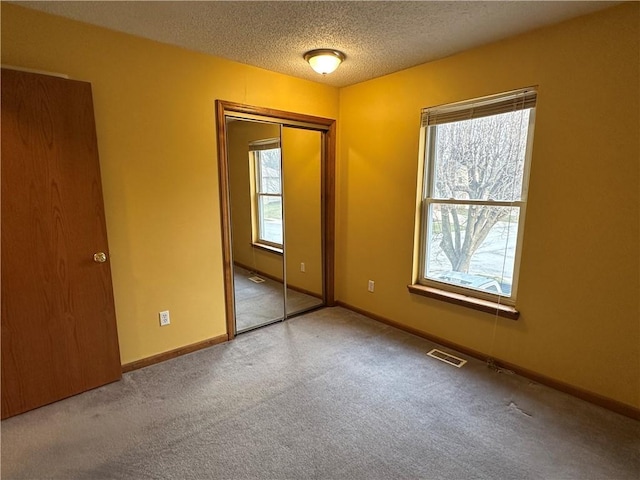 unfurnished bedroom featuring multiple windows, carpet, visible vents, and a textured ceiling