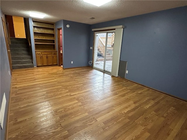 interior space featuring built in features, light wood-style floors, stairs, and a textured ceiling