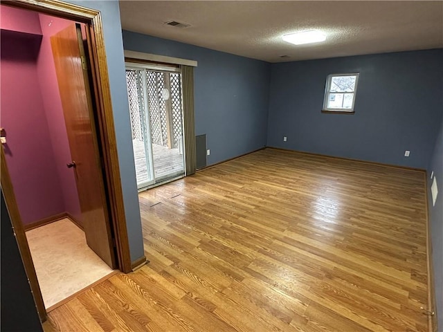 empty room featuring visible vents, a textured ceiling, and light wood-type flooring