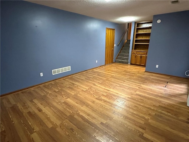 interior space featuring visible vents, built in shelves, a textured ceiling, wood finished floors, and stairs