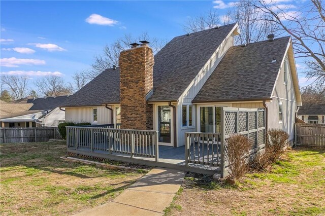rear view of house with a shingled roof, a deck, a chimney, and fence