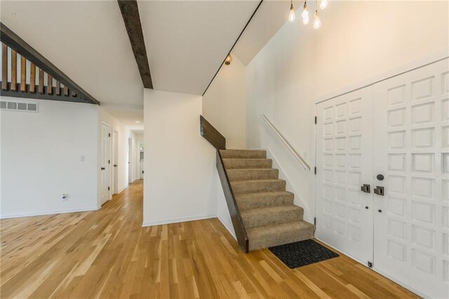 foyer entrance with stairway, visible vents, baseboards, light wood-style flooring, and beamed ceiling