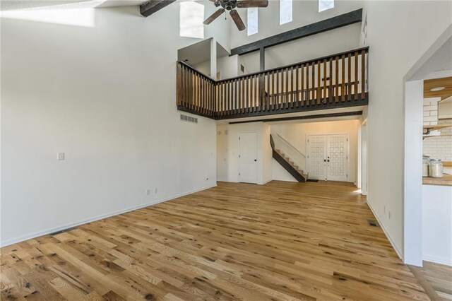 unfurnished living room with stairway, a high ceiling, ceiling fan, and wood finished floors