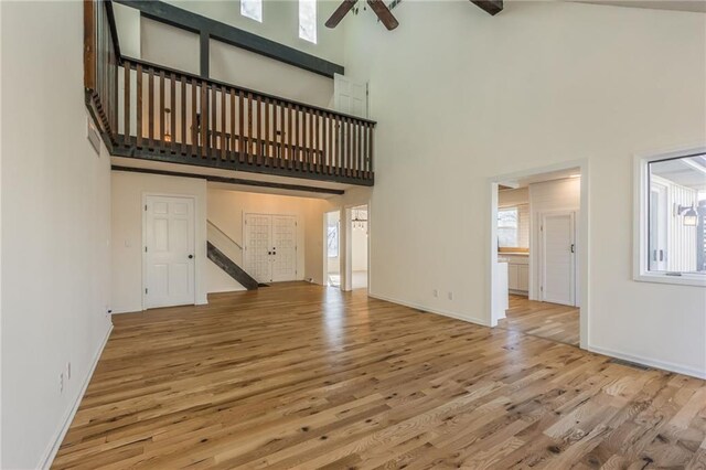 unfurnished living room featuring a ceiling fan, plenty of natural light, wood finished floors, and a towering ceiling