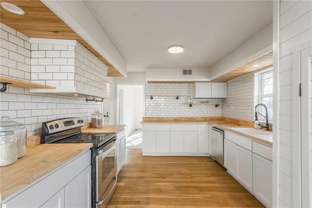 kitchen featuring open shelves, butcher block countertops, appliances with stainless steel finishes, and a sink