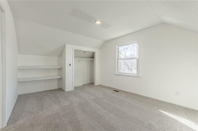 additional living space featuring visible vents, light carpet, a textured ceiling, and vaulted ceiling