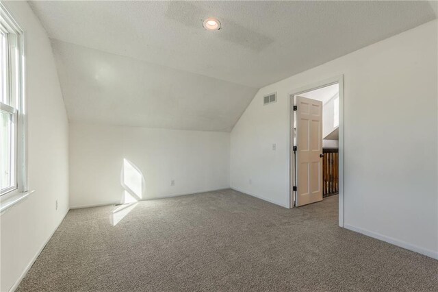 bonus room featuring vaulted ceiling, carpet flooring, visible vents, and a textured ceiling