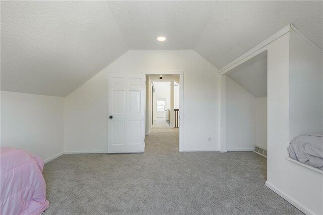unfurnished bedroom with lofted ceiling, carpet, visible vents, and a textured ceiling