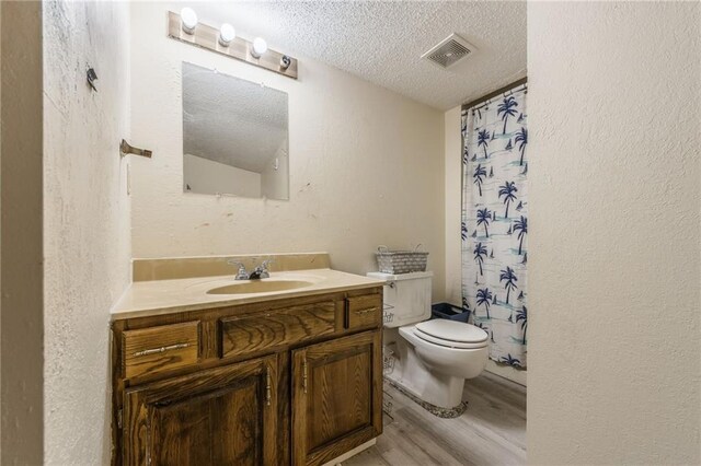 bathroom with visible vents, toilet, a textured ceiling, wood finished floors, and vanity