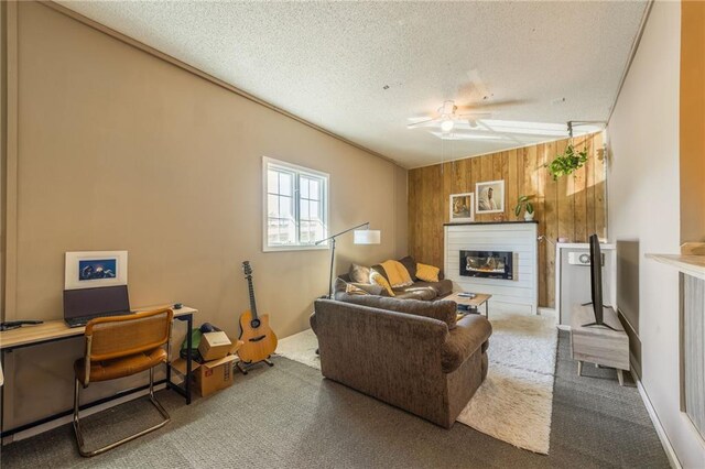 carpeted living area with wooden walls, a glass covered fireplace, a ceiling fan, and a textured ceiling