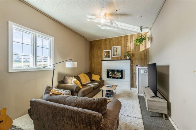 living room with wooden walls, ceiling fan, carpet flooring, a glass covered fireplace, and a textured ceiling