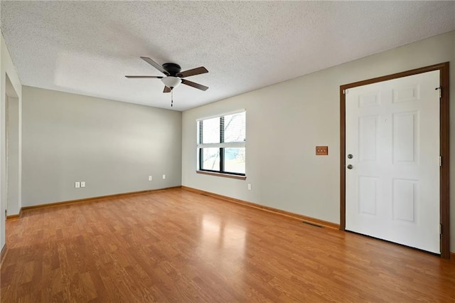 empty room with baseboards, light wood-style flooring, a textured ceiling, and ceiling fan