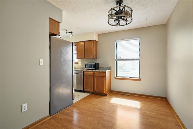 kitchen featuring light wood-type flooring, stainless steel appliances, a textured ceiling, and brown cabinetry