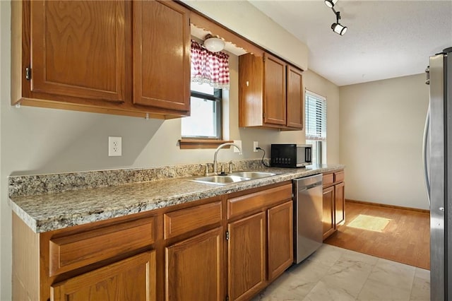 kitchen featuring brown cabinetry, marble finish floor, stainless steel appliances, and a sink