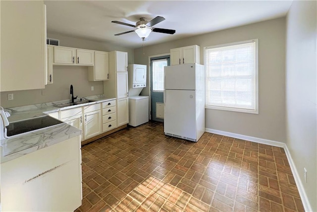 kitchen featuring stacked washer and clothes dryer, freestanding refrigerator, baseboards, and a sink