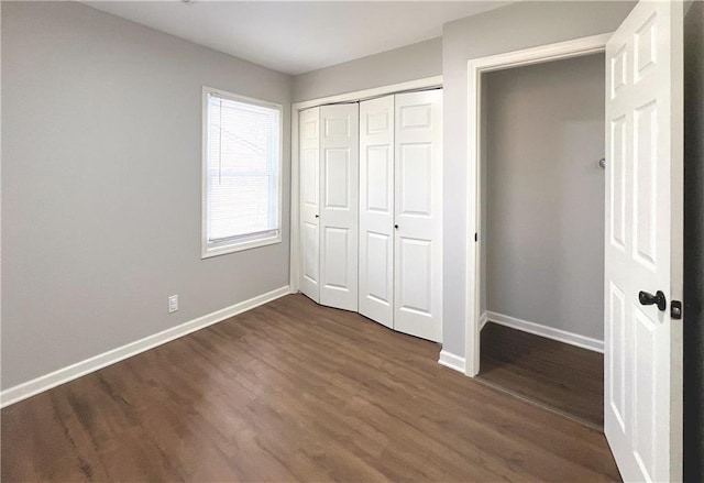 unfurnished bedroom with a closet, dark wood-type flooring, and baseboards