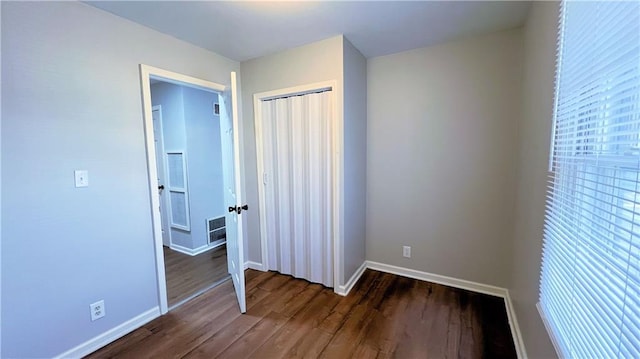 unfurnished bedroom with dark wood finished floors, visible vents, a closet, and baseboards