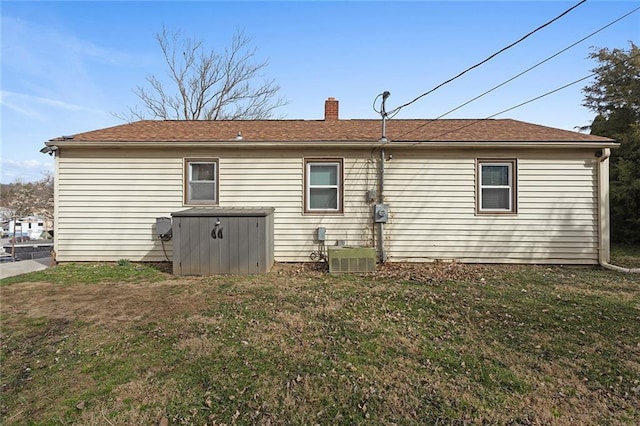 back of house with central air condition unit, a lawn, and a chimney