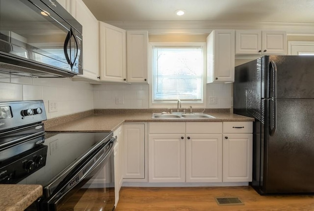 kitchen featuring tasteful backsplash, light wood-style floors, white cabinets, black appliances, and a sink